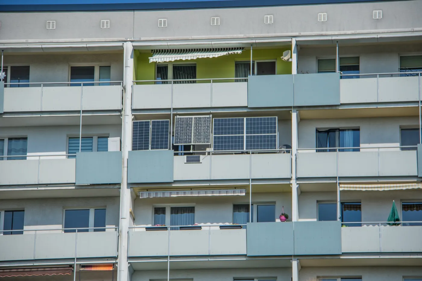 Several floors of a concrete apartment block, with solar panels hung on the railing of one balcony.