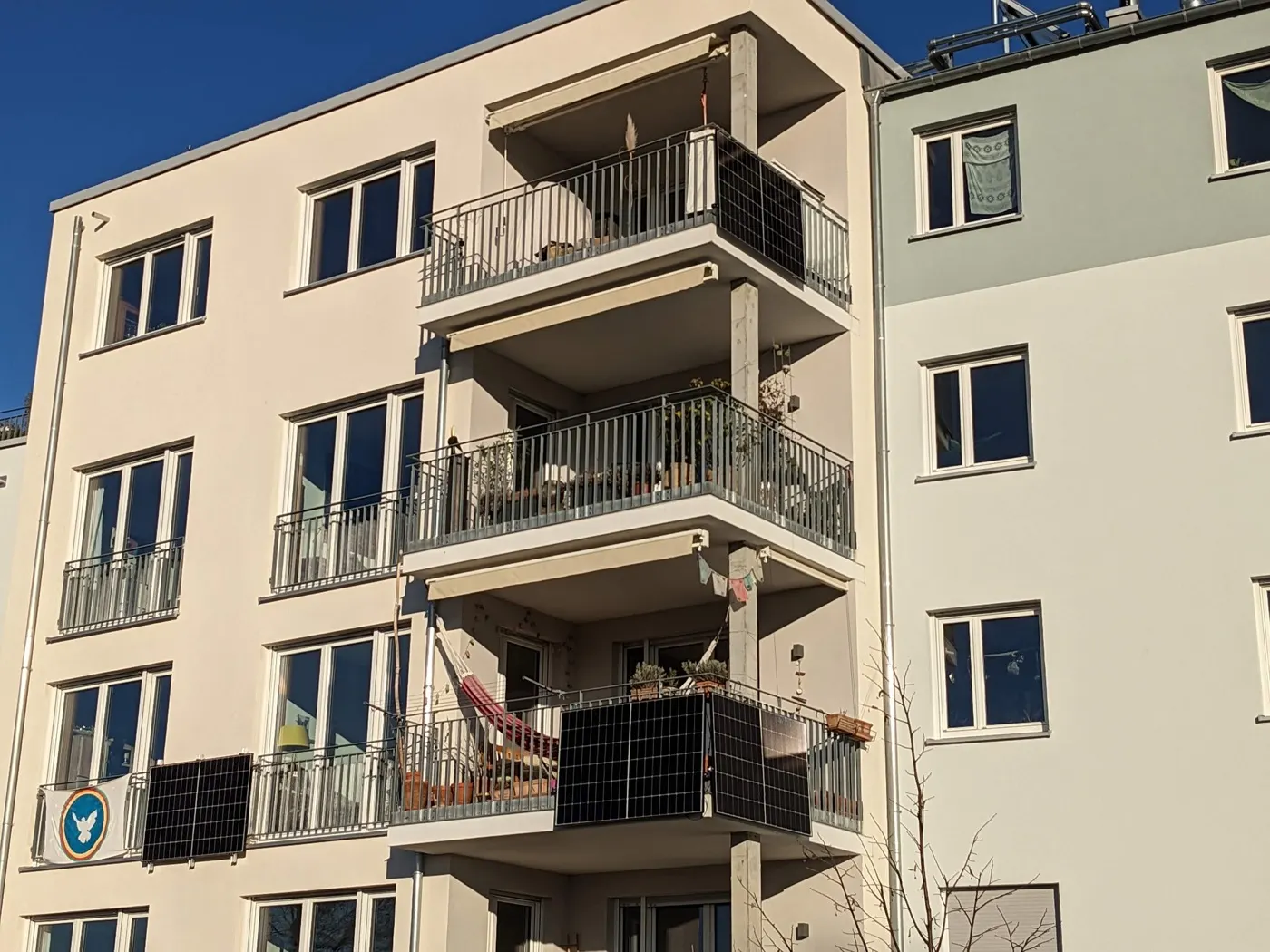 A cream apartment building under a blue sky, with black solar panels hung on the railings of three balconies.