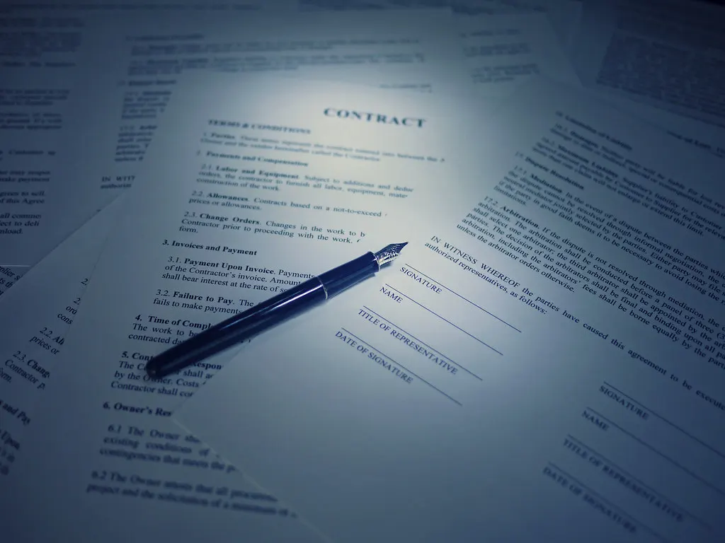 A printed contract with signature lines and a fountain pen resting on it.
