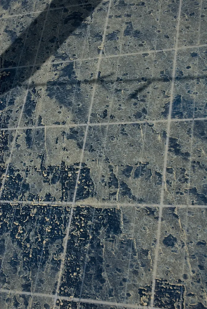 Close-up of a solar panel's cells caked in a thick, patchy layer of dust.