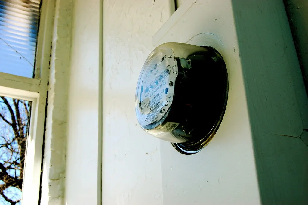 A round glass electric meter mounted on the white outside wall of a house.