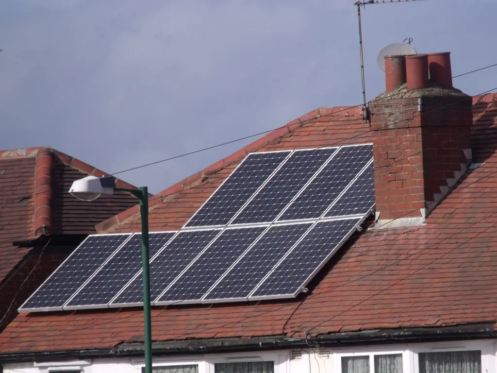 Two rows of solar panels on a red-tiled roof beside a chimney.
