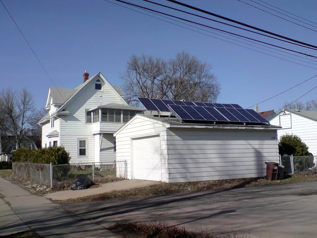 Solar panels on the roof of a detached garage next to a white two-story house.
