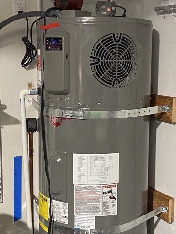 A Rheem heat pump water heater installed in a garage, with the fan grille on top where it draws in air.
